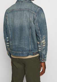 Jeansjacka i ljusblått med en urtvättad finish, med slitna detaljer och en knäppt krage. Bärs över en beige sweatshirt.