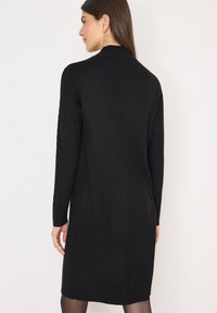 Abito maglione nero in maglia con maniche lunghe, bordo a costine e dettagli in maglia a trecce lungo le maniche. Silhouette aderente, lunghezza al ginocchio.
