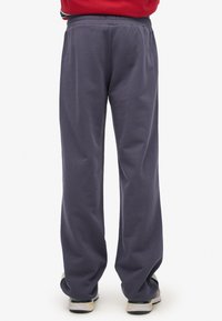 Marineblauwe katoenen joggingbroek met een elastische tailleband, rechte pijpen en een gladde textuur, gecombineerd met lichtgekleurde sneakers.