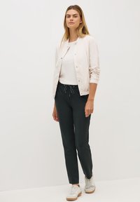 Veste bomber rose clair, top texturé blanc, pantalon noir fuselé avec cordon de serrage, et baskets beiges. Tenue simple et décontractée.