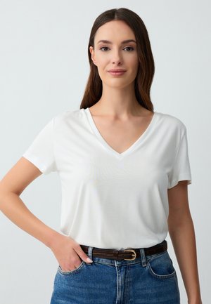 Witte korte mouwen V-hals t-shirt, zachte stof, relaxte pasvorm, gecombineerd met blauwe denim jeans en een bruine riem met een gouden gespaccent.