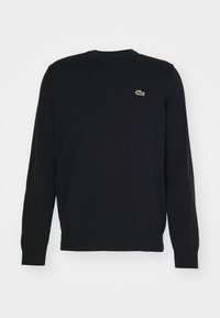 Pull noir à manches longues avec col rond, poignets et ourlet côtelés, arborant un petit logo crocodile vert et rouge brodé sur la poitrine gauche.