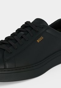 Baskets en cuir noir à lacets avec semelle épaisse, logo "BOSS" embossé en or sur le côté, couture soignée et col rembourré.