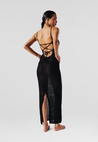 Schwarzes Maxikleid aus Mesh mit tiefem Rückenausschnitt, mit überkreuzten Trägern und seitlichen Schlitzen, das eine leichte und atmungsaktive Textur bietet.