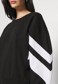 Sudadera negra con escote redondeado, de manga larga con rayas diagonales blancas y tejido texturizado. Puño en la cintura.
