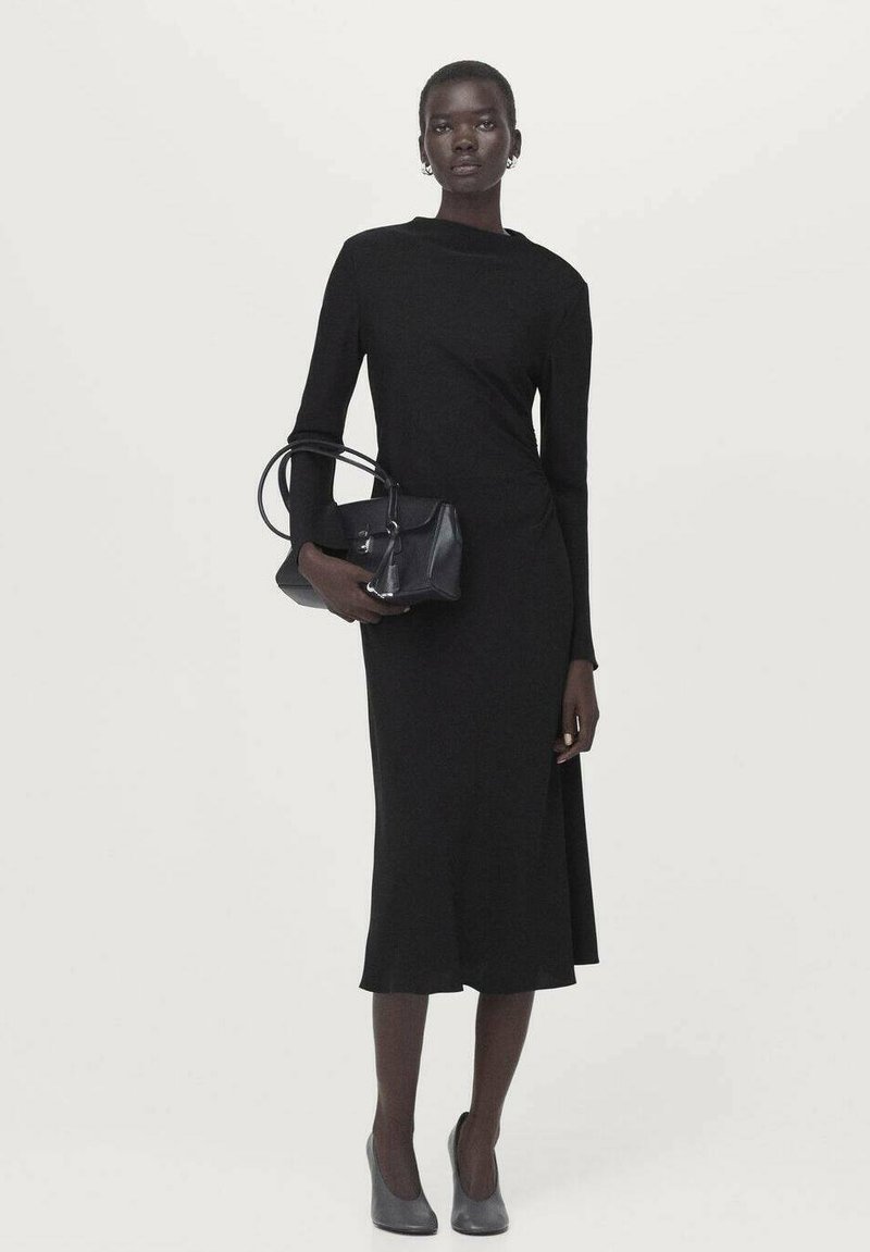 Rochie neagră cu mâneci lungi, cu corset strâns pe talie și tiv evazat, asortată cu o geantă mică neagră și pantofi cu toc înalt gri. Design simplu și elegant.