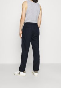 Marinblåa avslappnade byxor med dragsko i midjan, som har två bakfickor och är kombinerade med vita skor med gröna detaljer.