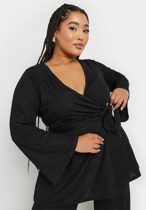 Black, textured wrap top with a deep V neckline and long bell sleeves, featuring a tie detail at the waist for a fitted silhouette.