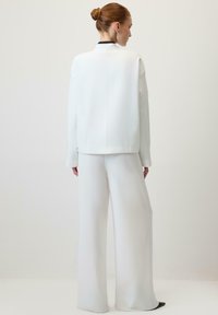 Hvid blazer og bukser med vide ben ses bagfra. Stoffet er glat med et struktureret design uden synlige lukninger eller mønstre.