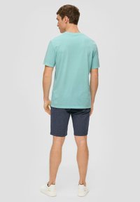 Lichtblauwe katoenen T-shirt met een ronde hals, gecombineerd met donkerblauwe gestreepte shorts en witte casual sneakers, gezien vanaf de achterkant.