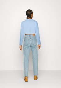 Camisa curta azul clara de botão combinada com jeans de cintura alta azul clara. O conjunto apresenta um corte descontraído e detalhes mínimos.