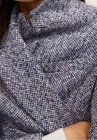 Tessuto testurizzato blu navy e bianco, con un motivo intrecciato. Presenta un design avvolgente con colletto alto e bordi ripiegati.