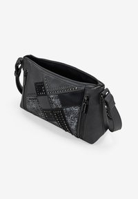 Bolso cruzado de imitación cuero negro con tachuelas, paneles texturizados y cierres de cremallera. Presenta un diseño geométrico y correa ajustable.