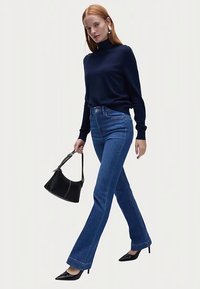 Maglione dolcevita blu scuro, jeans a zampa chiaro, borsa nera e scarpe con tacco nero. Tessuto liscio con linee pulite.