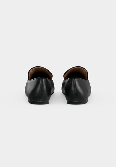 Paire de chaussures en cuir noir sans lacets, vues de dos sur un fond uni gris clair.