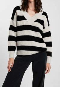Maglione lavorato a maglia a righe bianche e nere con scollo a V, caratterizzato da ampie righe orizzontali e polsini a coste. Tessuto strutturato, vestibilità comoda.