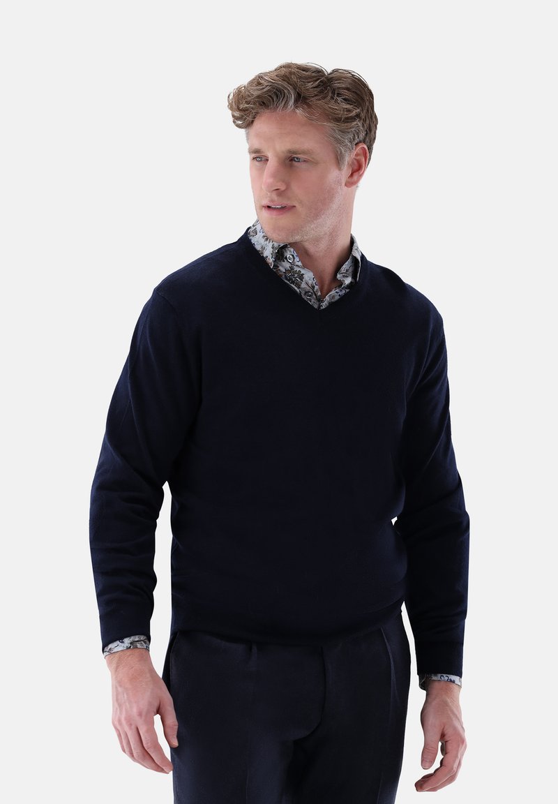 Marinefarbener V-Ausschnitt-Pullover aus weichem Strickstoff, mit langen Ärmeln und einem kontrastierenden, floral gemusterten Hemd darunter.