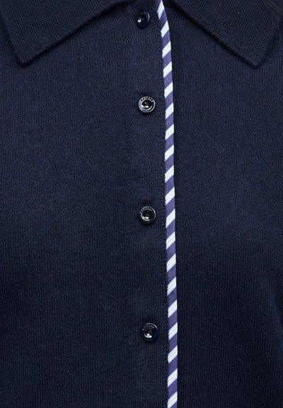 Σκούρο μπλε πλεκτό ζακέτα με μαύρα κουμπιά και ριγέ υφασμάτινη επένδυση κατά μήκος της γραμμής των κουμπιών, με μυτερό γιακά.