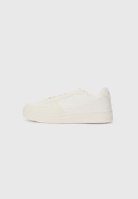 White sneaker with a smooth leather upper and suede accents. Features a perforated toe, flat laces, and a rubber sole with textured detailing.