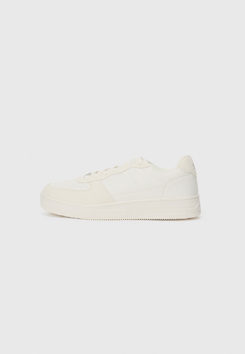 White sneaker with a smooth leather upper and suede accents. Features a perforated toe, flat laces, and a rubber sole with textured detailing.