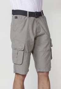 Shorts cargo gris en tissu léger. Comprend une ceinture noire, plusieurs poches latérales et une coupe décontractée.