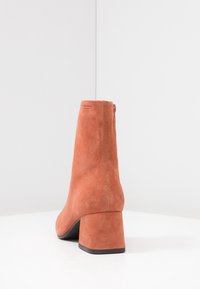 Suède enkellaars in brandweeroranje met een ronde neus, blokhak en achteraille. Glad textuur met minimale merkdetails.