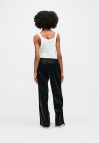 Μαύρο, λαμπερό παντελόνι με φαρδιές γραμμές και ελαστική μέση, σε συνδυασμό με λευκό, ραμμένο αμάνικο μπλουζάκι. Θέα από πίσω σε λευκό φόντο.