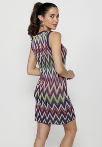 Rochie fără mâneci cu un model în zig-zag în nuanțe de roșu, verde și violet. Textură tricotată, formă ajustată și lungime până la mijlocul coapsei.