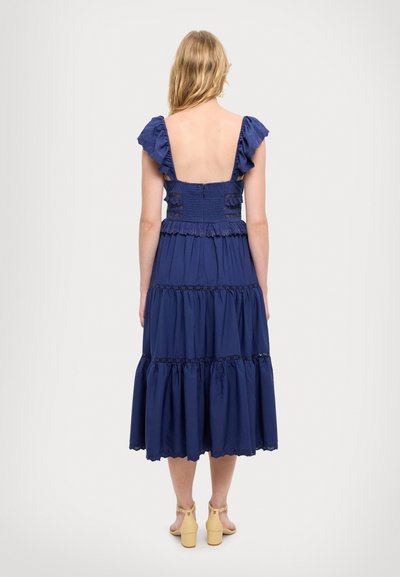 Navyblaues Baumwollkleid mit gestuften Rüschen, gerafftem Oberteil und offenem Rücken. Es hat eine Spitzenkante und eine voluminöse, fließende Silhouette.