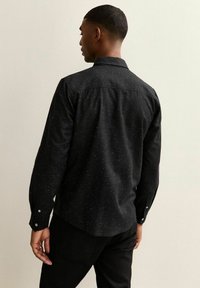 Zwarte lange mouwen shirt met een gestructureerd patroon, opgerolde manchetten en een subtiel gespoten ontwerp. Weergave toont de achterkant en kraag.