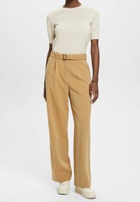 Beżowe szerokie spodnie z wysokim stanem i szlufkami na pasek, połączone z kremowym swetrem z dzianiny z detalicznym wzorem koronkowym na rękawach.