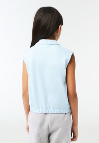Světlomodrý bezrukávový polo top vyrobený z měkké látky, s límečkem a volným střihem, s žebrovaným lemem a hladkou texturou.