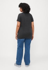 T-shirt gris à manches courtes, col rond et fentes sur les côtés, assorti à un jean en denim bleu ample et des baskets grises. Détails de couture subtils.