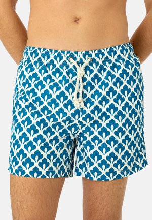 Gros plan sur une personne portant un short de bain à motifs bleus et blancs avec un cordon blanc noué à la taille.