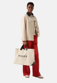 Beige wool blend jacket with black collar, black buttons, and pockets. Red pants. Canvas tote bag with black handles and BOGNER logo.