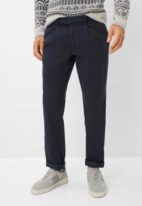 Marineblauwe chinos met een recht gesneden ontwerp, voorzien van een sluiting met een knoop aan de voorkant, zijzakken en opgerolde mouwen, gecombineerd met grijze sneakers.