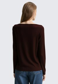 Bordeaux geribbelde longsleeve top met een wijde halslijn, aansluitend ontwerp en zachte textuur, gecombineerd met lichtblauwe denimjeans.