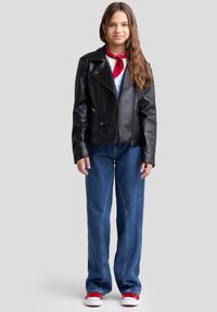 Giacca da moto in pelle nera con tasche con zip e automatiche, indossata sopra una camicia azzurro chiaro, abbinata a jeans larghi di denim e sneakers rosse.