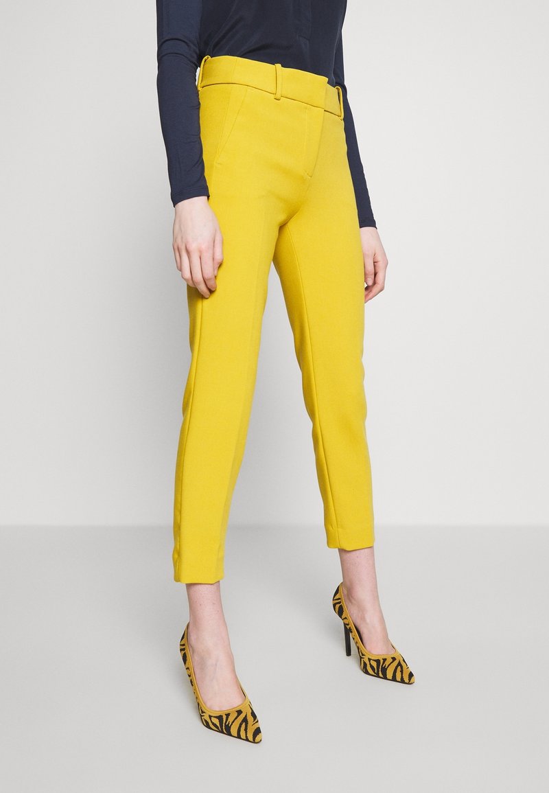 Geel gepaste broek met een slim fit en riemlussen. Draag met zwart-geel gestreepte hoge hakken. Soepele stofstructuur.