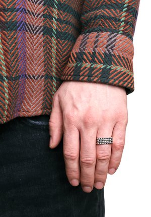 Gewebtes Hemd mit einem orangen, grünen und braunen Fischgrätmuster; schwarze Jeans; Hand geschmückt mit einem silbernen Ring mit erhobenen Bändern.
