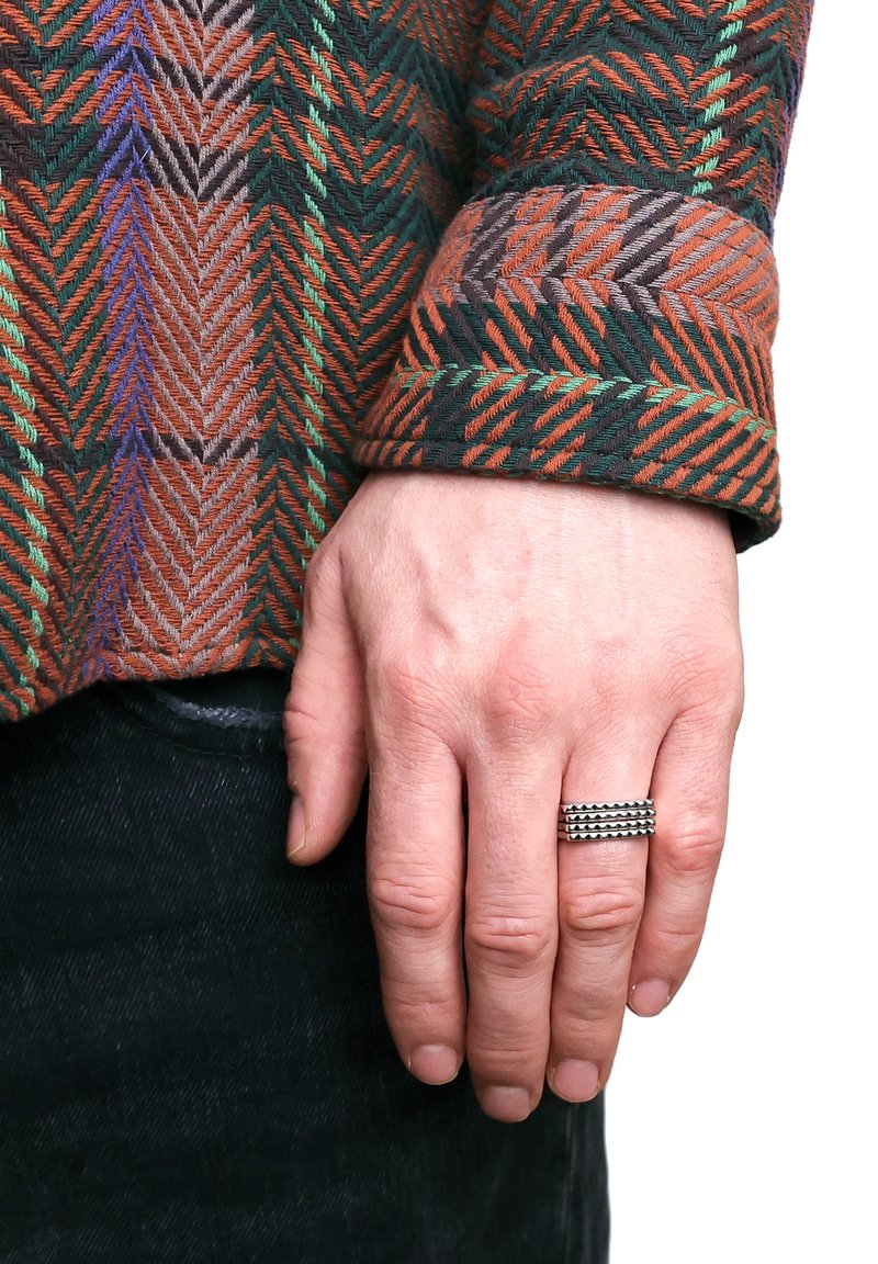 Gewebtes Hemd mit einem orangen, grünen und braunen Fischgrätmuster; schwarze Jeans; Hand geschmückt mit einem silbernen Ring mit erhobenen Bändern.