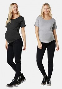 Topuri de maternitate din amestec de bumbac gri închis și gri deschis, cu mâneci scurte și laterale plisate, purtate cu blugi skinny negri și ghete până la gleznă.
