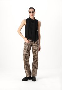 Blouse noire sans manches avec un détail de nœud au cou, associée à un pantalon beige à imprimé zèbre et des chaussures à plateforme noires.