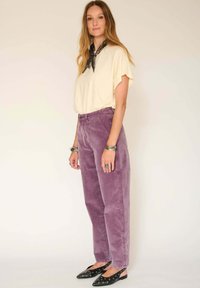 Haut beige clair à manches courtes associé à un pantalon en velours côtelé lavande ample taille haute et des chaussures noires à enfiler avec des embellissements.