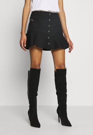 Zwarte denim minirok met een uitlopende zoom en metalen knopen aan de voorkant. Gecombineerd met hoge, zwarte suède over-de-knee laarzen.