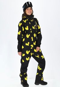 Zwart skibestand met een herhalend patroon van gele rubberen eenden, voorzien van een ritssluiting aan de voorkant, zakken en verstelbare manchetten; gecombineerd met zwarte skibril.