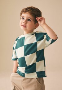 Zelena in kremasta kratasta majica s kratkimi rokavi iz mehke tkanine. Obla vratni izrez z raztegljivim krojem in podrobnostjo etikete na bočnem šivu.