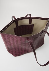 Hluboká burgundská taška přes rameno s jemným geometrickým vzorem. Kožený vnější materiál, podšívka uvnitř a zapínání na zip s dvojitými madly pro snadné nošení.