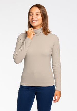 Maglietta a maniche lunghe color beige chiaro con collo alto, design aderente, texture liscia, tessuto morbido; abbinata a jeans blu, estetica minimalista.