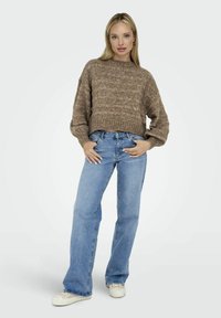 Pull en tricot marron avec un ourlet côtelé, associé à un jean bleu clair et des baskets blanches. Le pull présente un motif texturé et des manches larges.